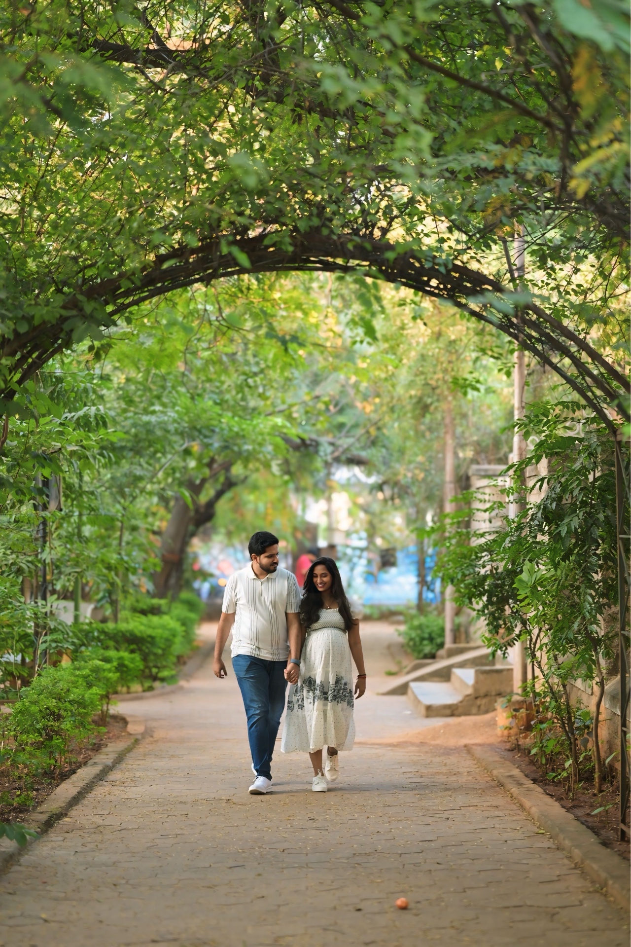 Expecting parents walking hand in hand under a green archway