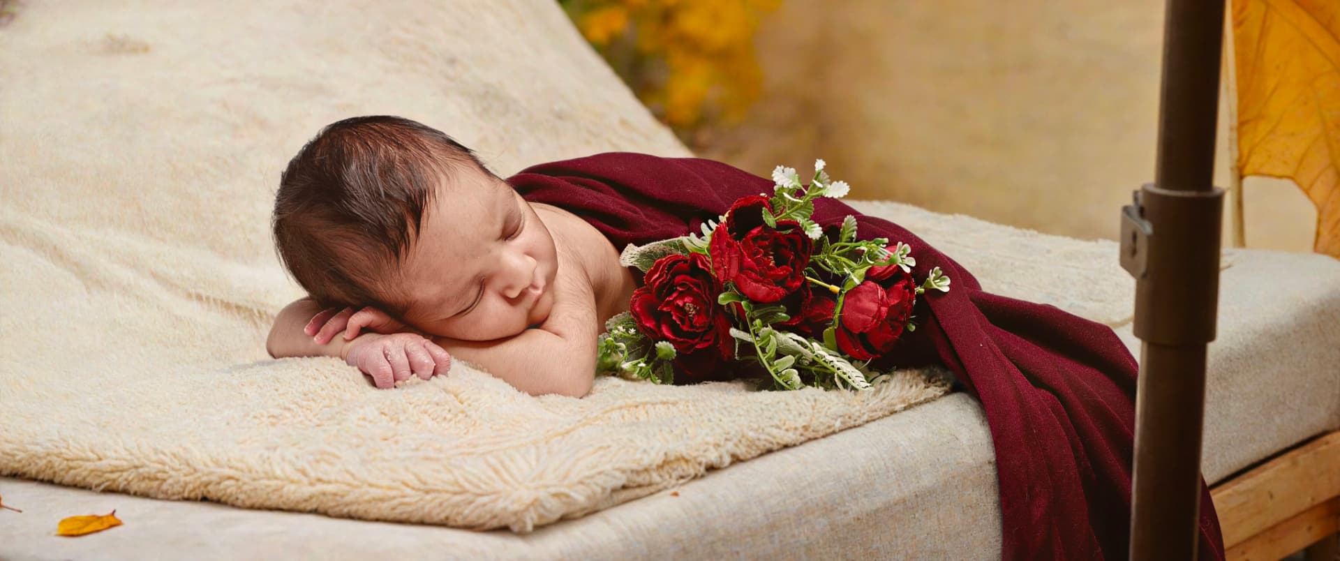 Newborn wrapped in deep red beside roses