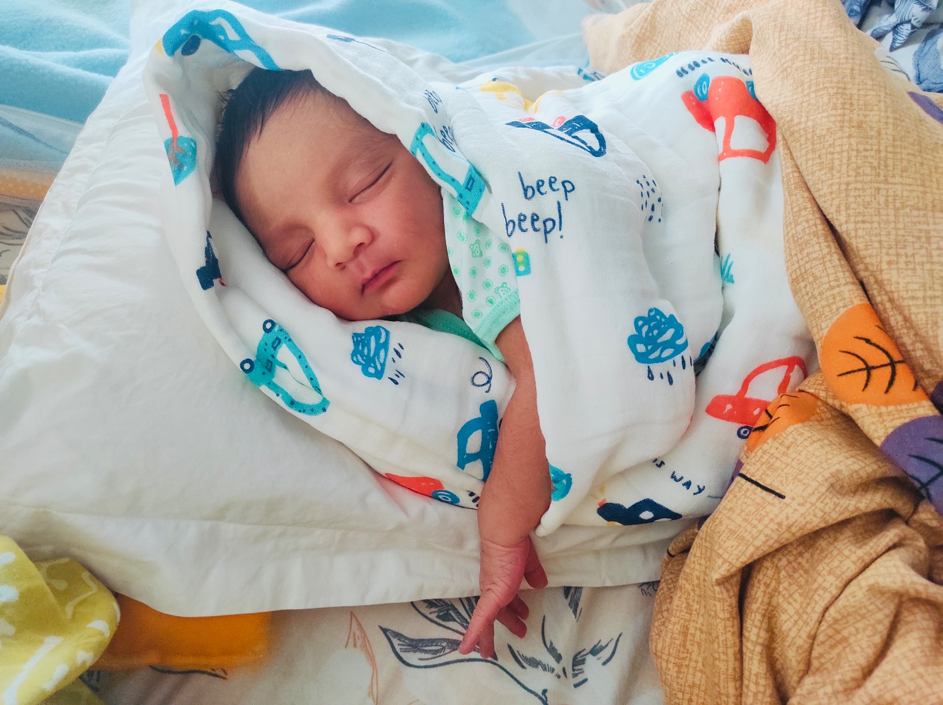 Newborn asleep wrapped in a printed muslin blanket
